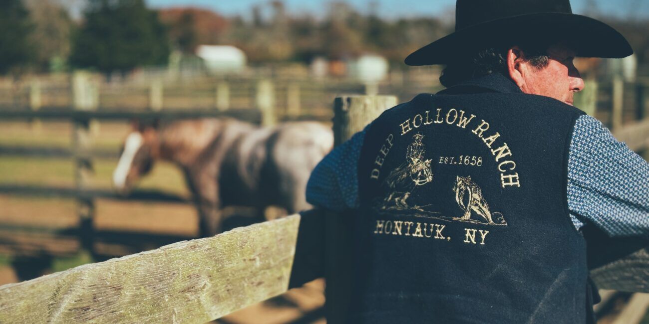 A wrangler at the corral fence in a Deep Hollow Ranch vest