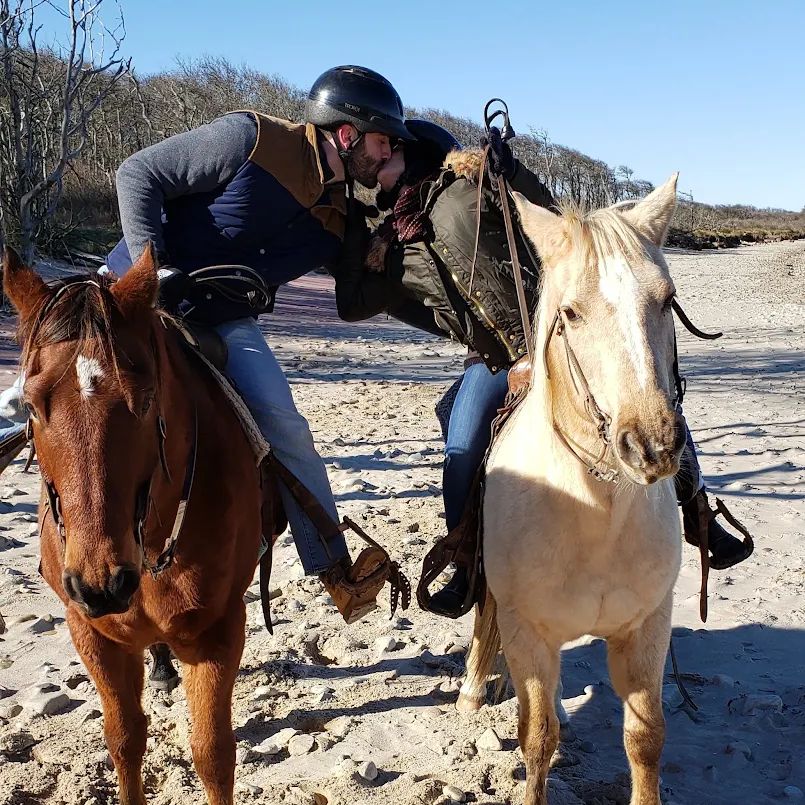 A couple sharing a kiss on horseback on the beach